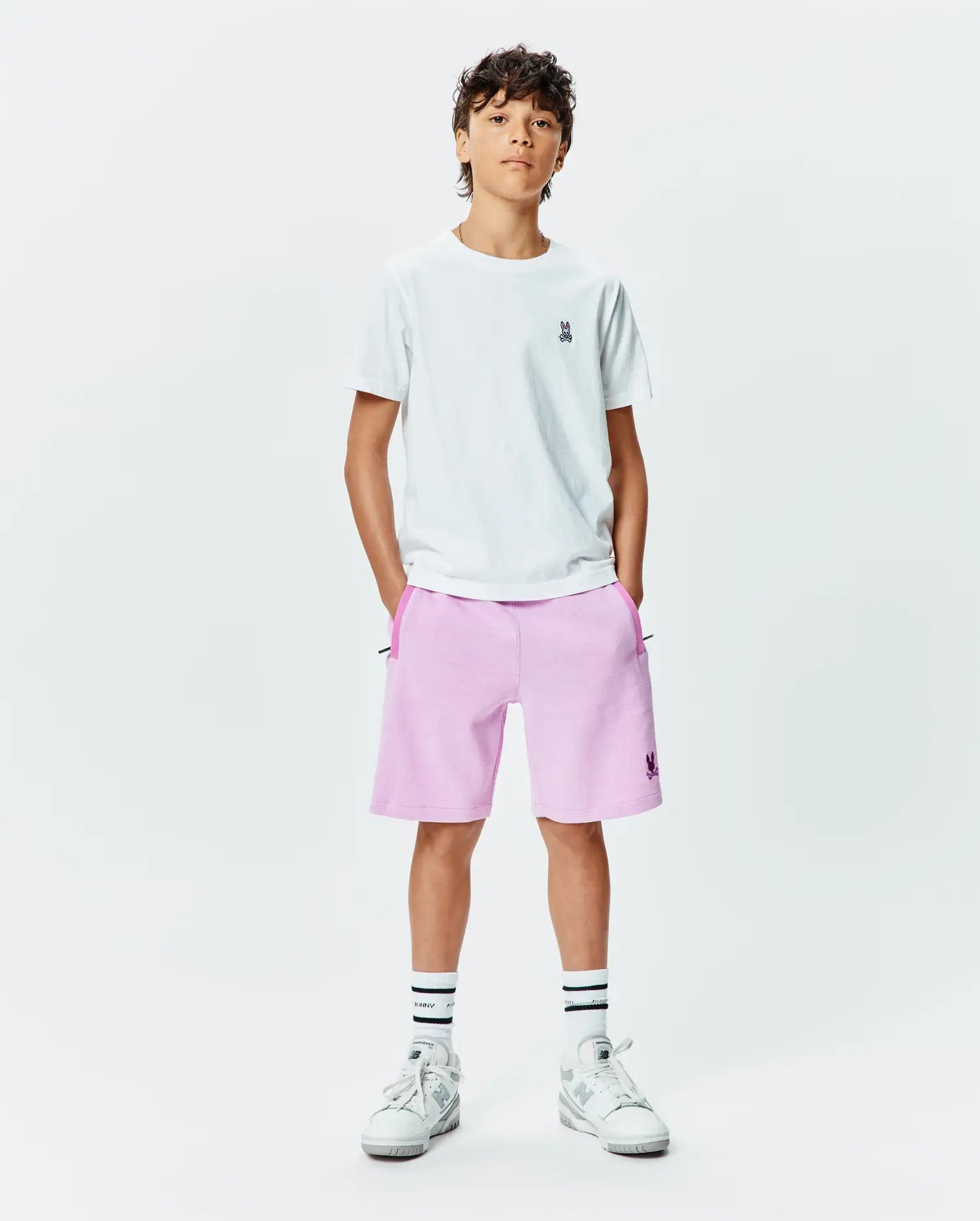 White jersey t-shirt with small embroidered Psycho Bunny logo on left chest, paired with Kids Keith Short 3 1/2 in light pink french terry, featuring a larger embroidered Psycho Bunny logo on the left leg and dark pink pocket trim.