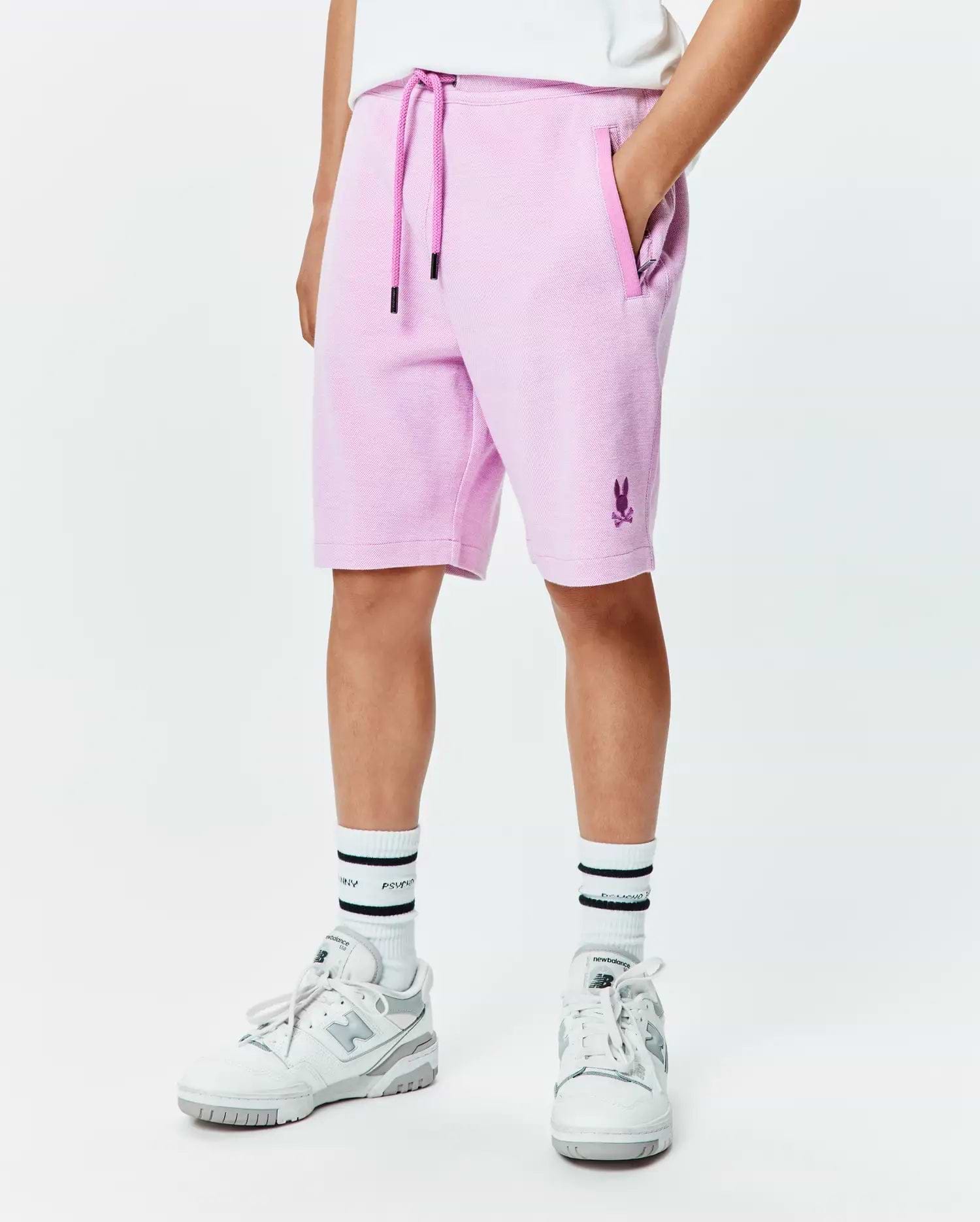 Kids Keith Short, a relaxed fit lavender pique short featuring a dark purple drawstring, side pockets, and a small embroidered Psycho Bunny skull logo on the lower left leg.