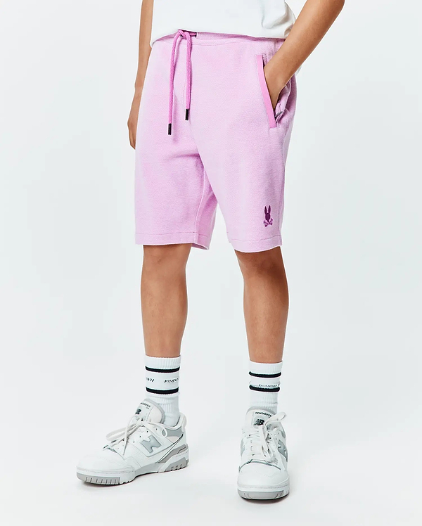 Kids Keith Short, a relaxed fit lavender pique short featuring a dark purple drawstring, side pockets, and a small embroidered Psycho Bunny skull logo on the lower left leg.
