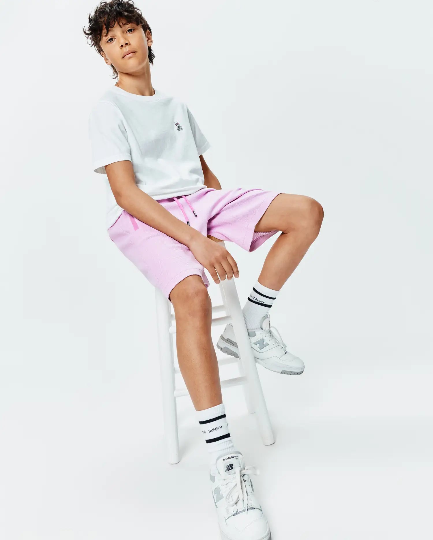 White classic fit jersey t-shirt with small embroidered Psycho Bunny skull logo on left chest, paired with relaxed fit pink French terry Kids Keith Short 3 1/2 featuring pink drawstrings.