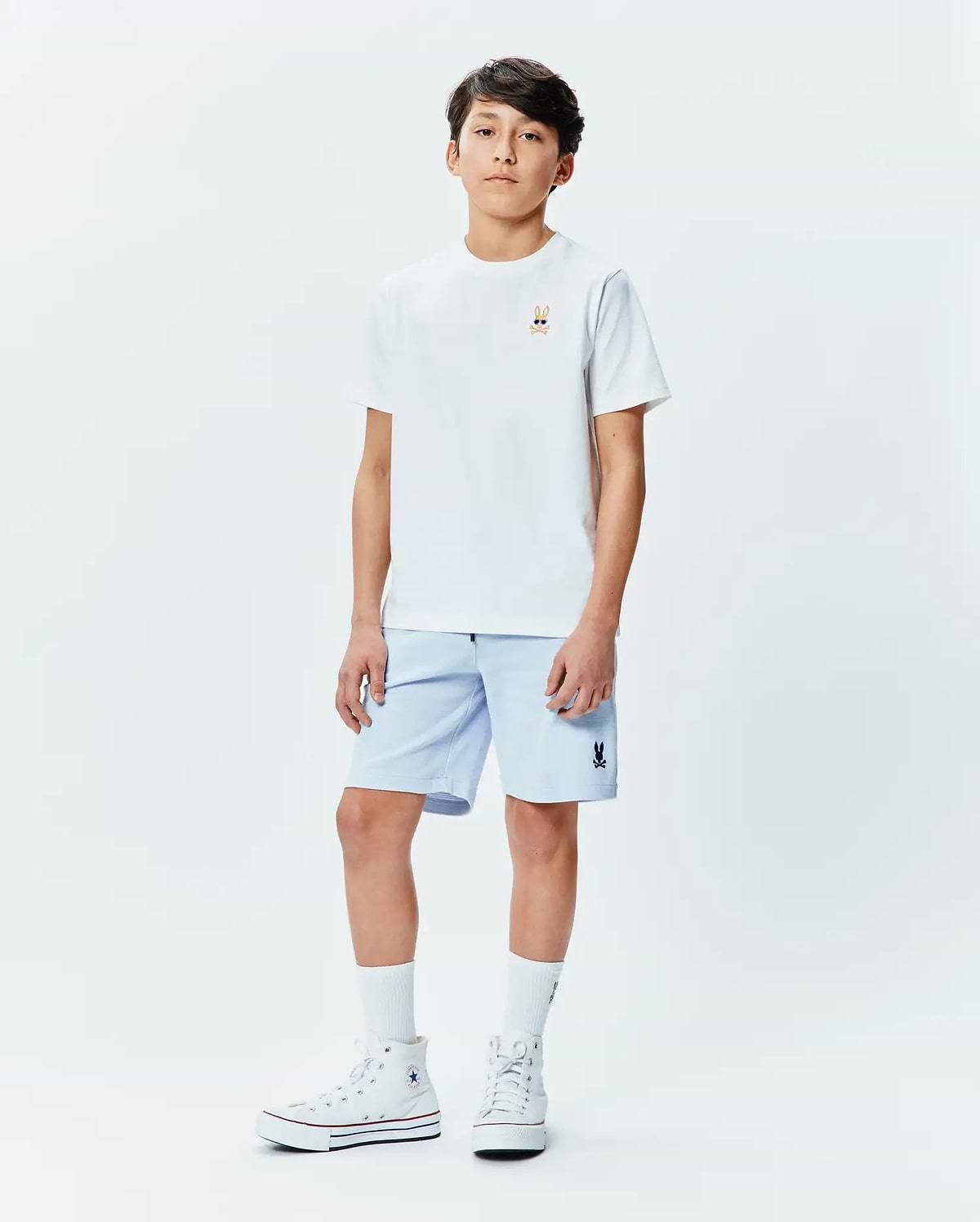 White classic fit jersey t-shirt with a small embroidered Psycho Bunny skull logo wearing sunglasses on the left chest, paired with light blue Kids Keith Short 3 1/2 with a small embroidered Psycho Bunny logo on the left leg. (4)