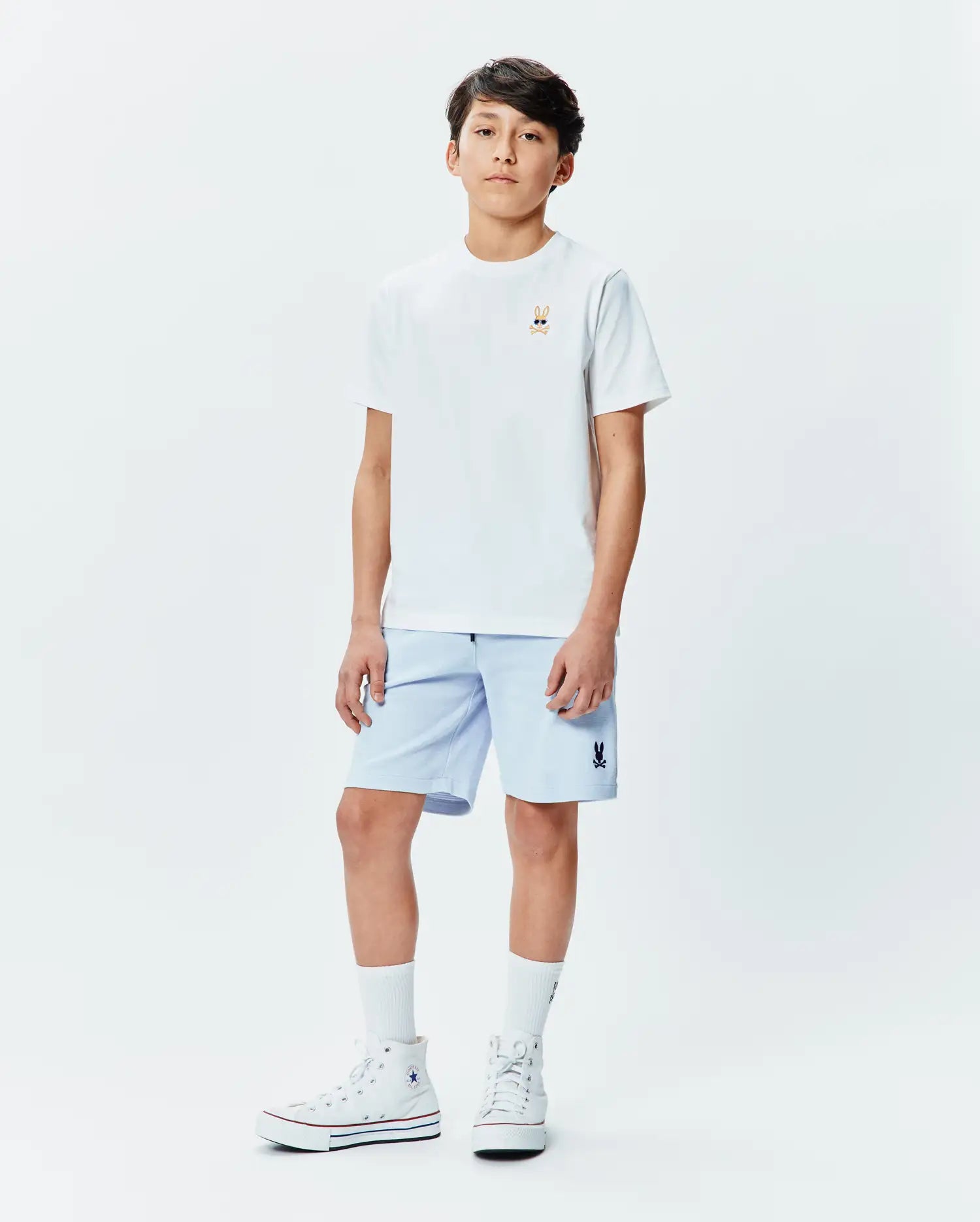 White classic fit jersey t-shirt with a small embroidered Psycho Bunny skull logo wearing sunglasses on the left chest, paired with light blue Kids Keith Short 3 1/2 with a small embroidered Psycho Bunny logo on the left leg. (4)