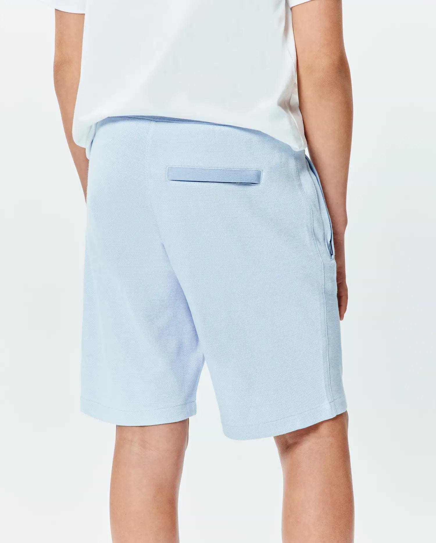 Light blue Kids Keith Short by Psycho Bunny, a relaxed pique knit with a back pocket featuring darker blue trim and side pockets. (3)