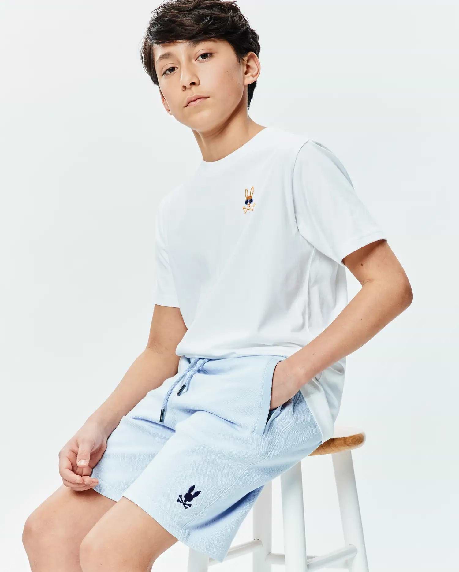 White classic fit jersey t-shirt with small embroidered Psycho Bunny sunglasses logo on chest. Light blue pique Kids Keith Short 3 1/2 with drawstring waist and small dark blue embroidered Psycho Bunny logo on leg. (2)