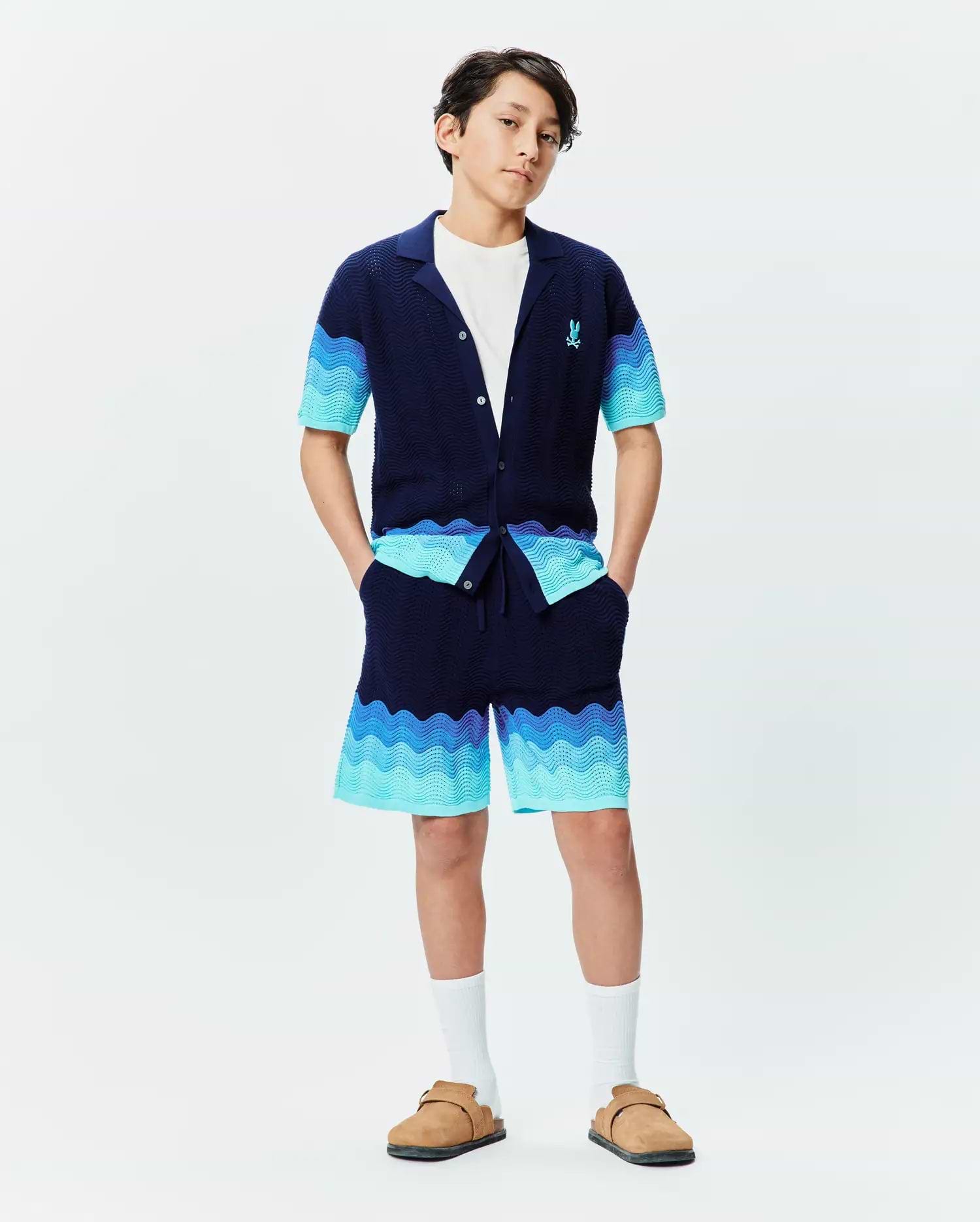 Psycho Bunny navy knit collared shirt and Kids Holden Knit Short set, featuring a wavy gradient pattern in blues and turquoise, textured knit fabric, and a small embroidered blue bunny skull logo on the left chest. (4)