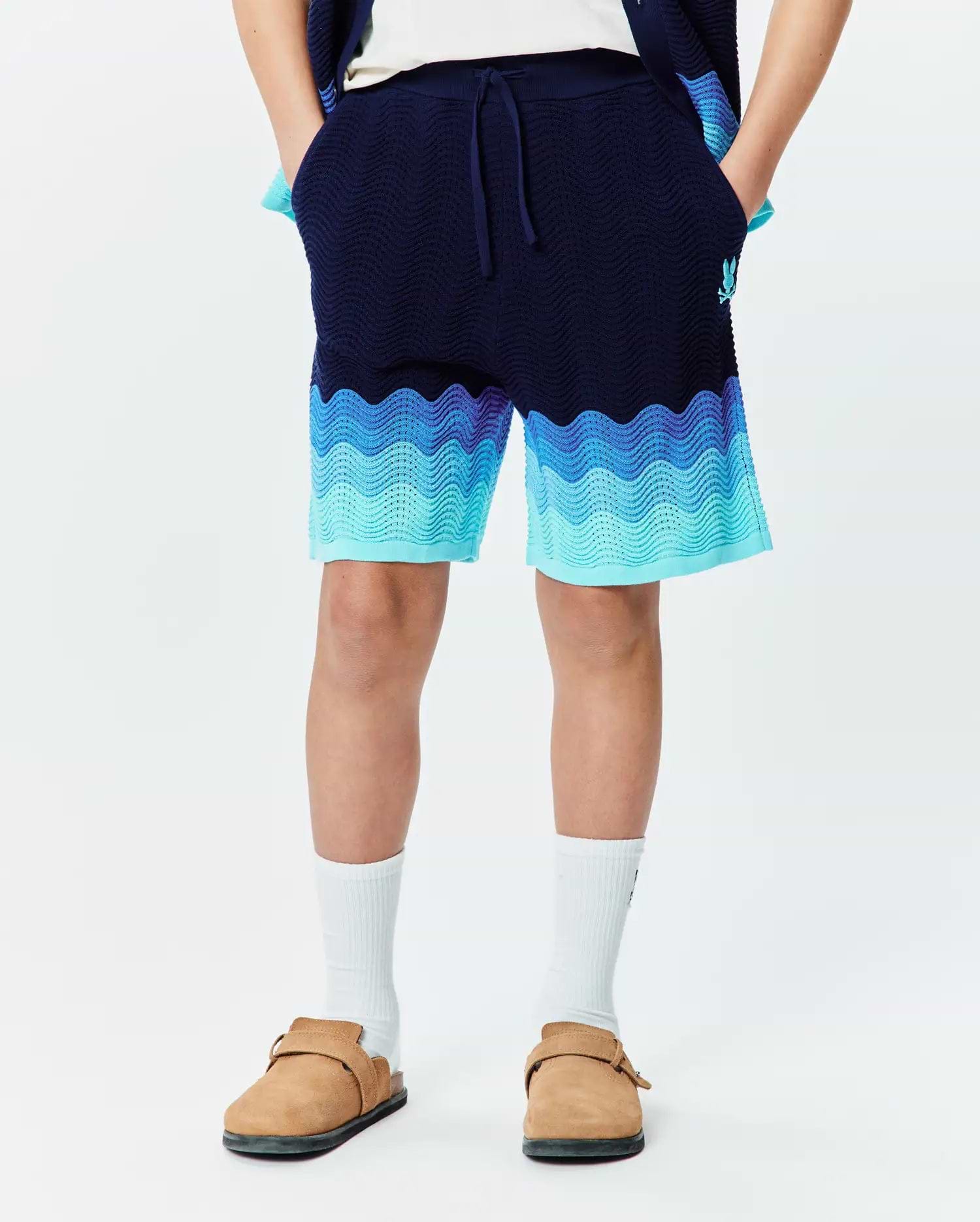 Kids Holden Knit Short in navy blue with a relaxed fit, featuring a wavy gradient pattern in light blue and aqua, textured knit fabric, and a small embroidered Psycho Bunny skull logo on the left leg. (1)