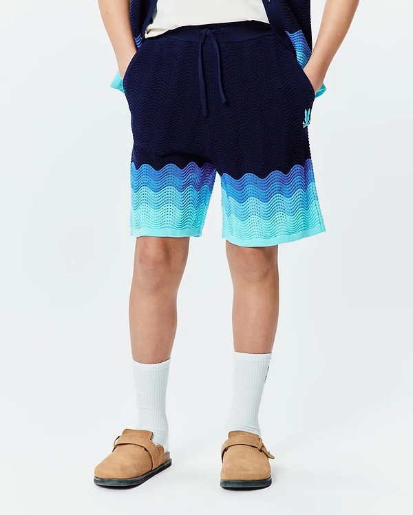 Kids Holden Knit Short in navy blue with a relaxed fit, featuring a wavy gradient pattern in light blue and aqua, textured knit fabric, and a small embroidered Psycho Bunny skull logo on the left leg.