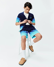Navy blue knit short-sleeve shirt and Kids Holden Knit Short set featuring a wavy blue gradient pattern, with a small embroidered Psycho Bunny skull logo on the shirt's left chest. (3)
