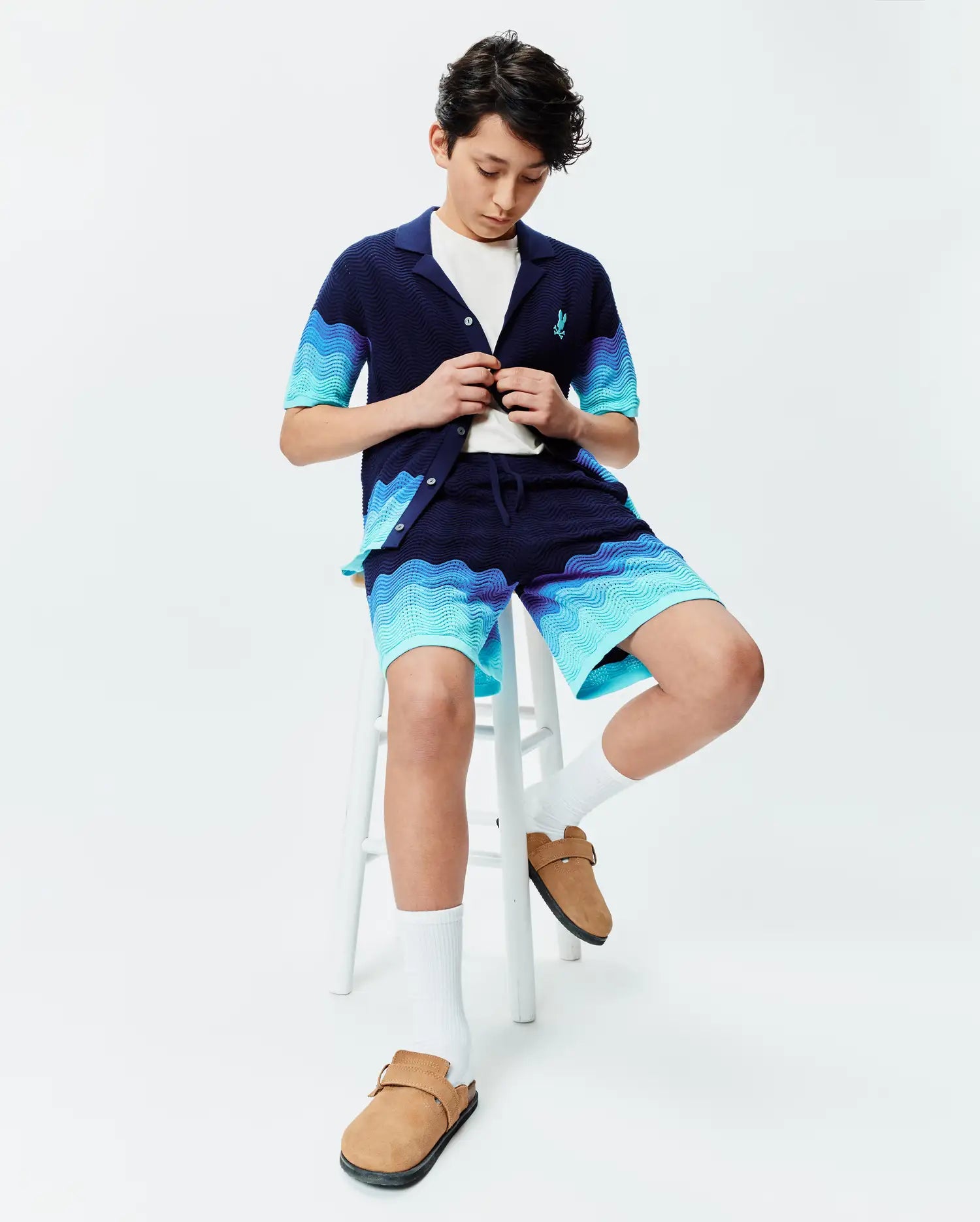 Navy blue knit short-sleeve shirt and Kids Holden Knit Short set featuring a wavy blue gradient pattern, with a small embroidered Psycho Bunny skull logo on the shirt's left chest. (3)