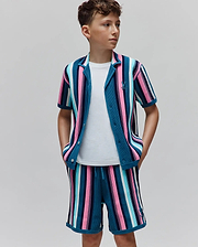 Kids Cliff Knit Shirt and matching shorts, featuring vibrant teal, pink, blue, white vertical stripes. Classic fit textured knit with small embroidered Psycho Bunny skull logo on chest and shorts.