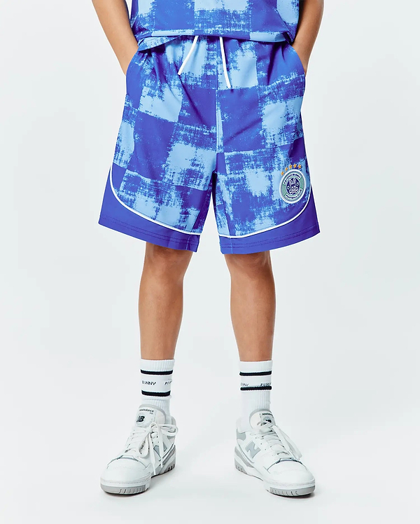 Kids Micah Soccer Short in blue and light blue distressed checkered pattern, smooth athletic fabric, white piping, relaxed fit, and a large Psycho Bunny Football Club patch on the left leg.