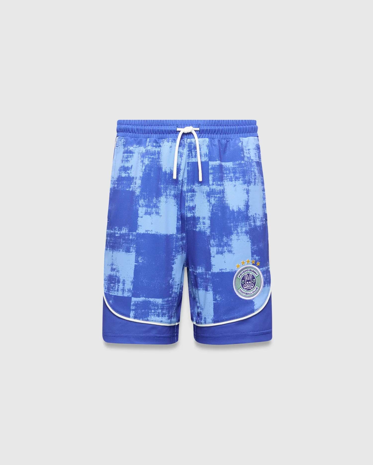 Kids Micah Soccer Short in blue with a distressed light blue checkered pattern, white drawstring, and white piping. Features a circular Psycho Bunny Football Club logo with a bunny skull and stars on the right leg.