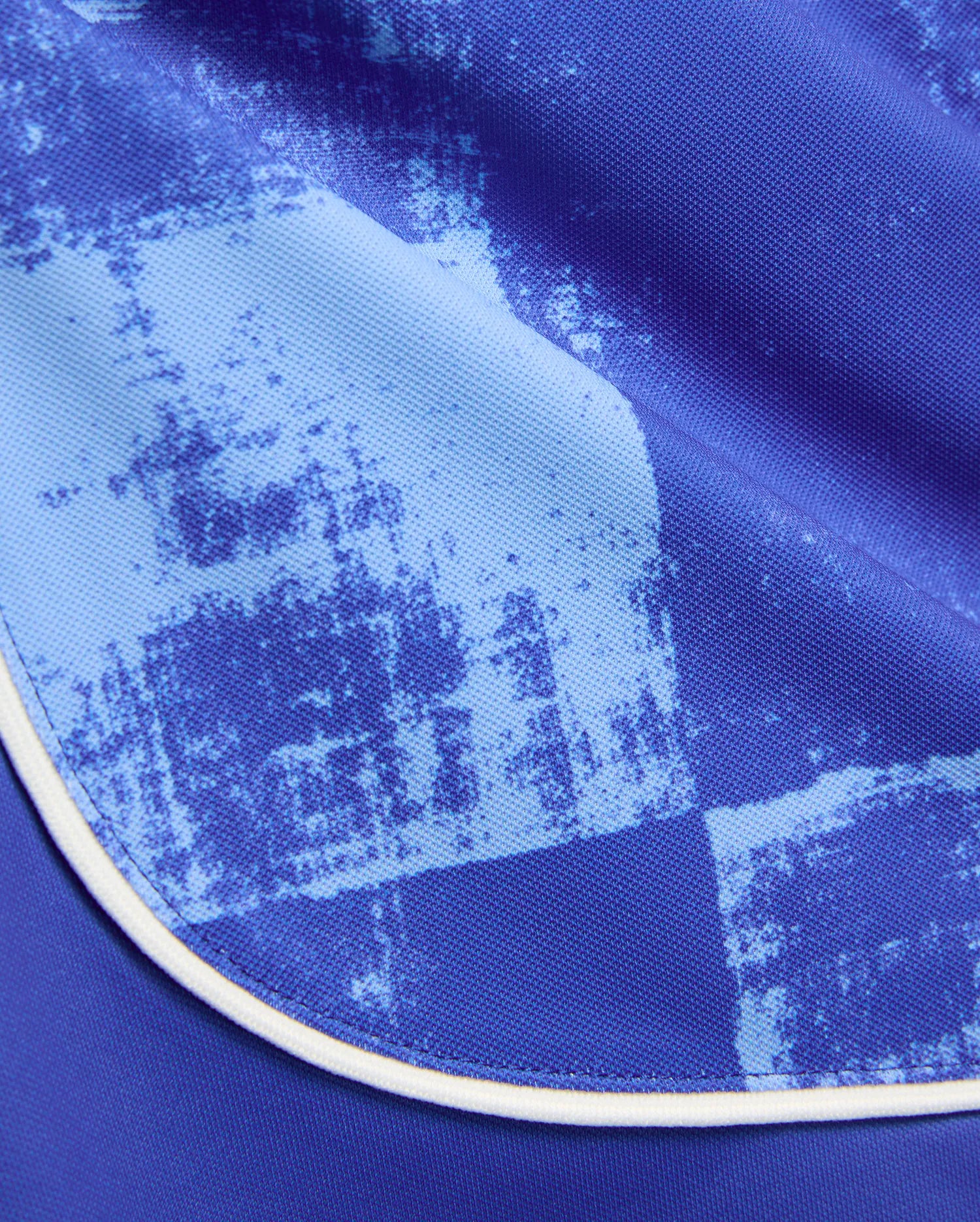 Kids Micah Soccer Short featuring a royal blue pique knit fabric with an abstract light blue distressed splatter pattern and crisp white piping along the curved hem.