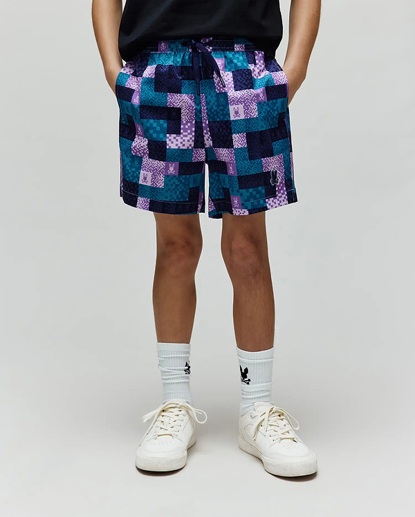 Kids Olivier All Over Bunny Swim Trunk in a relaxed fit, featuring a vibrant teal, purple, and navy patchwork pattern with small integrated Psycho Bunny skull logos throughout. Smooth, quick-dry fabric.