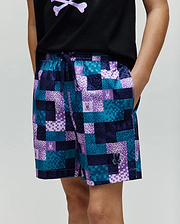 Kids Olivier All Over Bunny Swim Trunk with a vibrant pixelated teal, dark blue, and purple checkered pattern, featuring small bunny skull logos and a rubberized Psycho Bunny logo on the lower left leg.