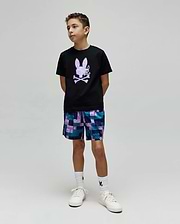 Black classic-fit jersey t-shirt with a large lavender Psycho Bunny skull graphic on the chest, paired with Kids Olivier All Over Bunny Swim Trunk, a blue and purple patchwork short with small bunny logos.