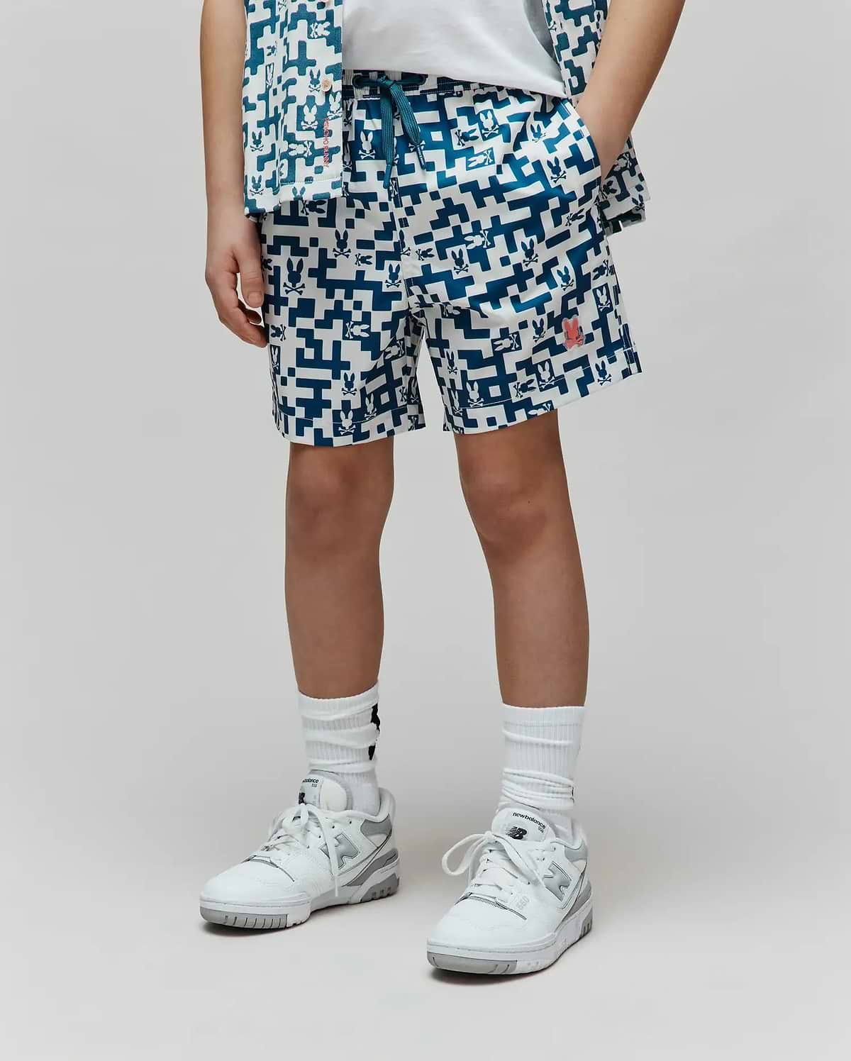 Kids Josh Swim Trunk, white with a deep blue pixelated pattern of repeating Psycho Bunny skull logos, a prominent red bunny logo on the right leg, and a relaxed fit in quick-dry fabric. (1)