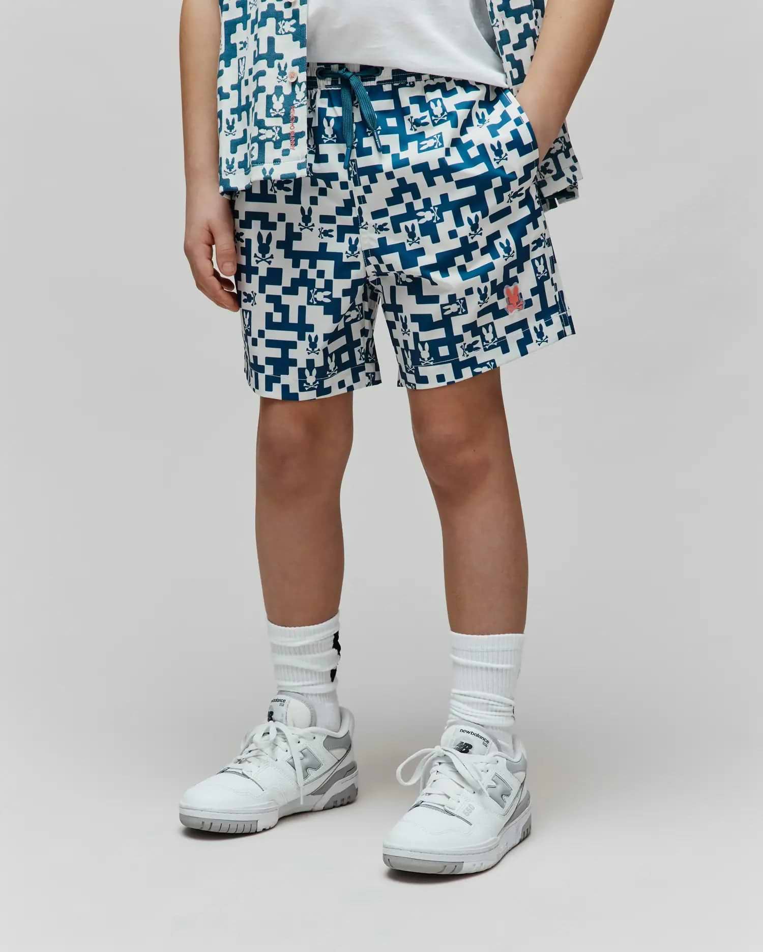 Kids Josh Swim Trunk, white with a deep blue pixelated pattern of repeating Psycho Bunny skull logos, a prominent red bunny logo on the right leg, and a relaxed fit in quick-dry fabric. (1)
