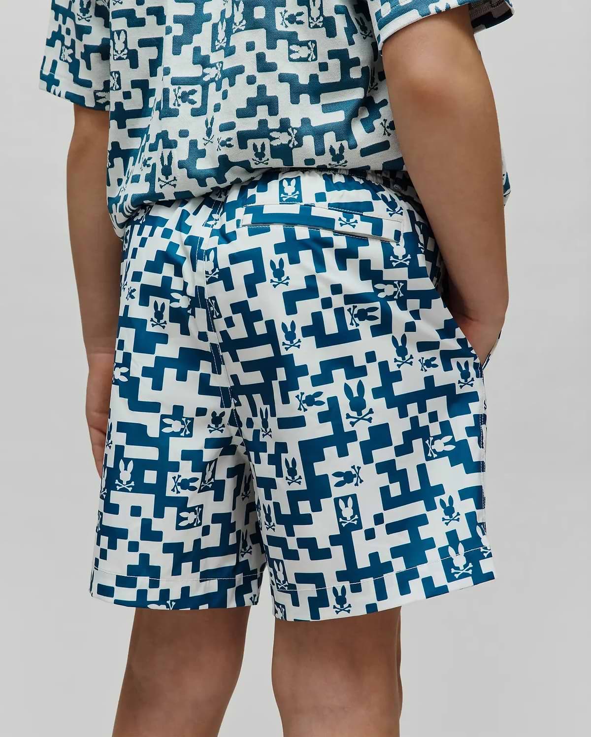 Kids Josh Swim Trunk in white with a teal pixelated geometric pattern featuring small Psycho Bunny skull logos throughout, a classic fit, and smooth quick-dry fabric. (3)