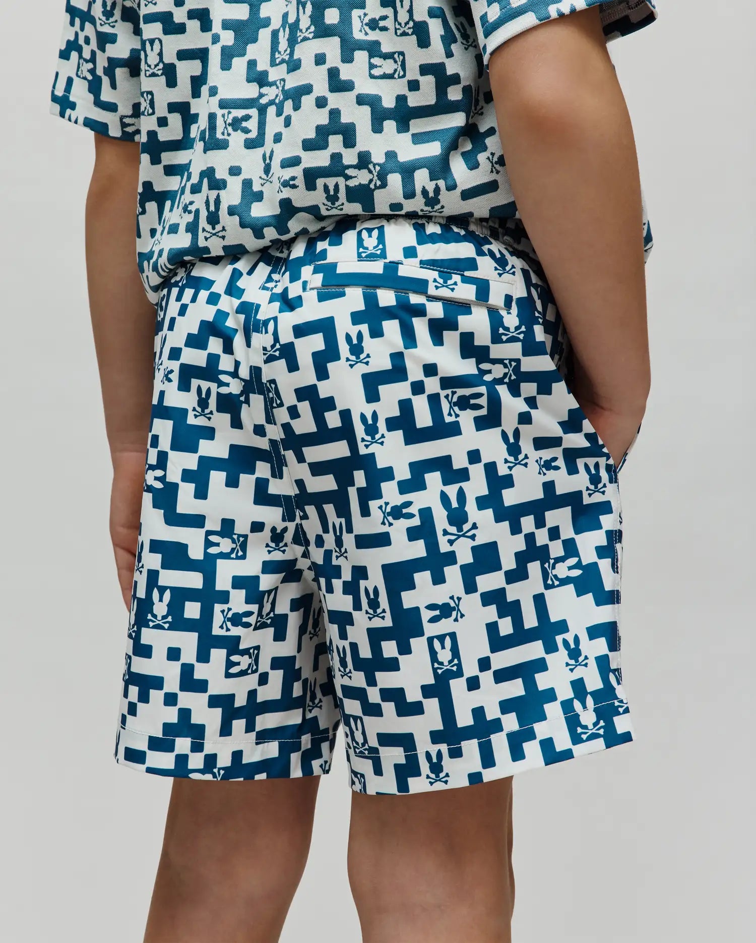 Kids Josh Swim Trunk in white with a teal pixelated geometric pattern featuring small Psycho Bunny skull logos throughout, a classic fit, and smooth quick-dry fabric. (3)