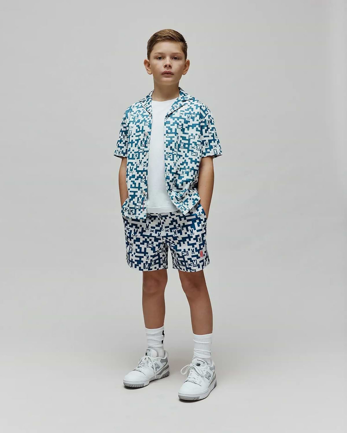Kids Josh Swim Trunk and matching short-sleeve button-up shirt in a white and teal pixelated pattern featuring the Psycho Bunny skull logo, with a small red logo on the trunk, all in a relaxed fit. (4)