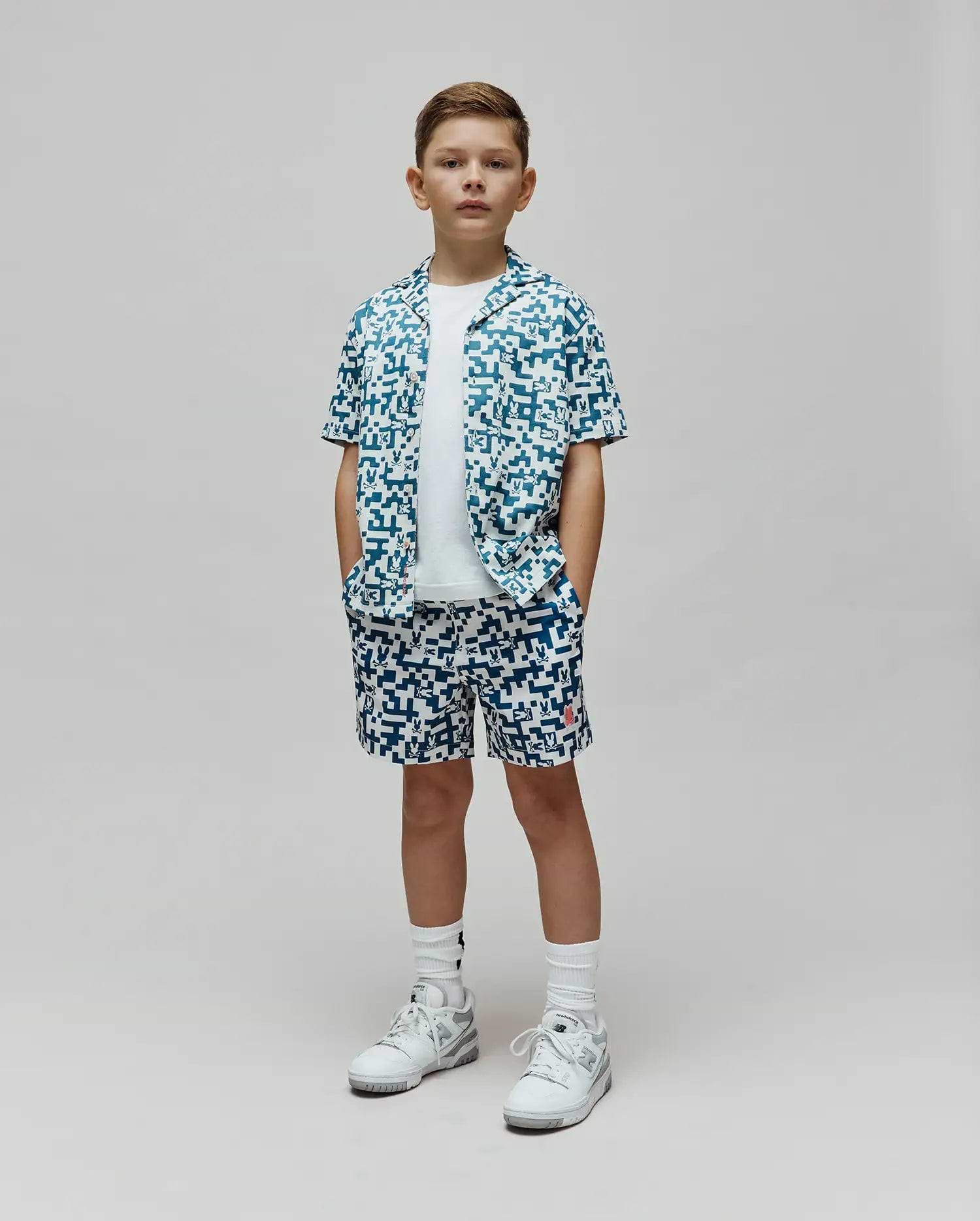 Kids Josh Swim Trunk and matching short-sleeve button-up shirt in a white and teal pixelated pattern featuring the Psycho Bunny skull logo, with a small red logo on the trunk, all in a relaxed fit. (4)