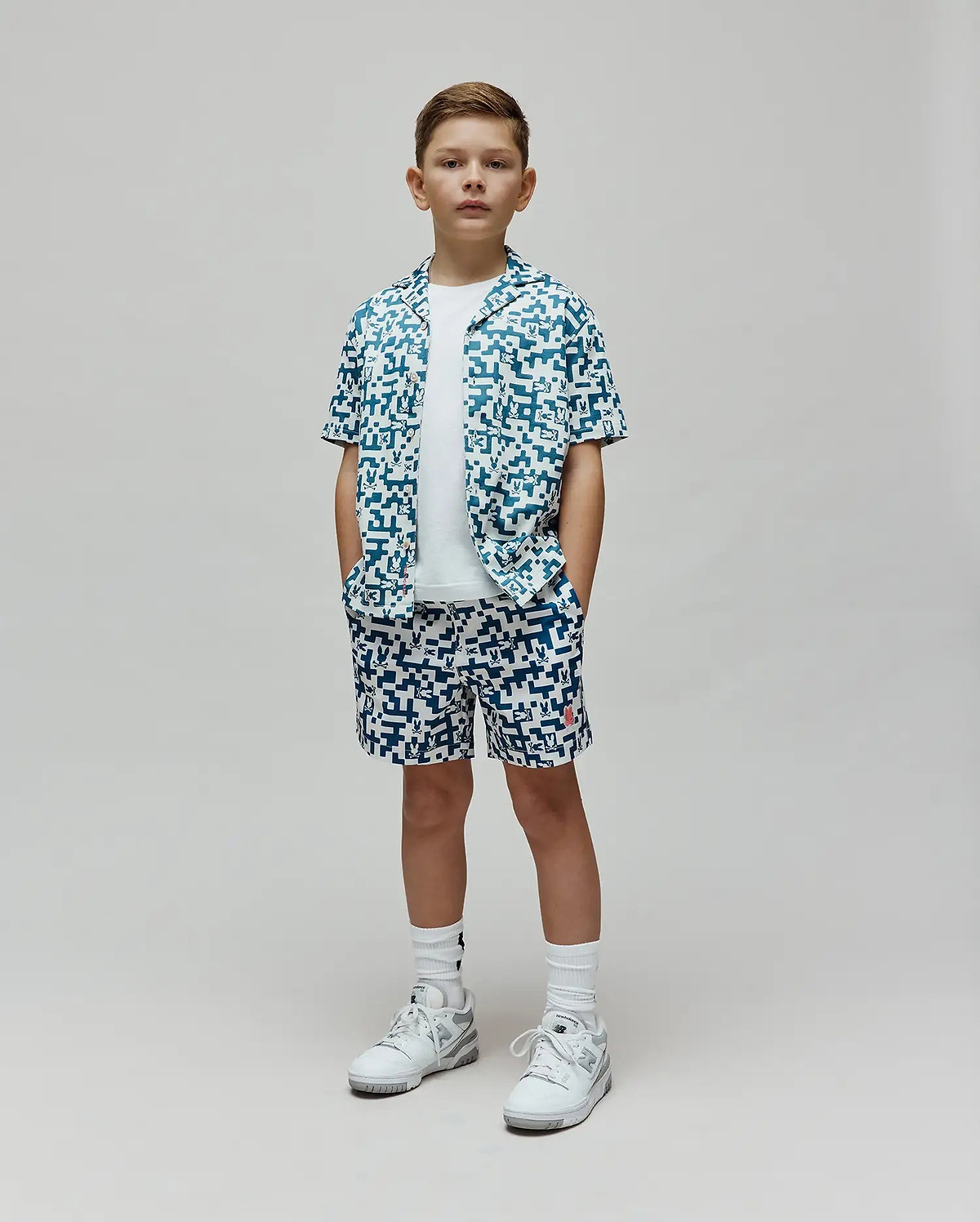 Kids Josh Swim Trunk and matching short-sleeve button-up shirt in a white and teal pixelated pattern featuring the Psycho Bunny skull logo, with a small red logo on the trunk, all in a relaxed fit. (4)