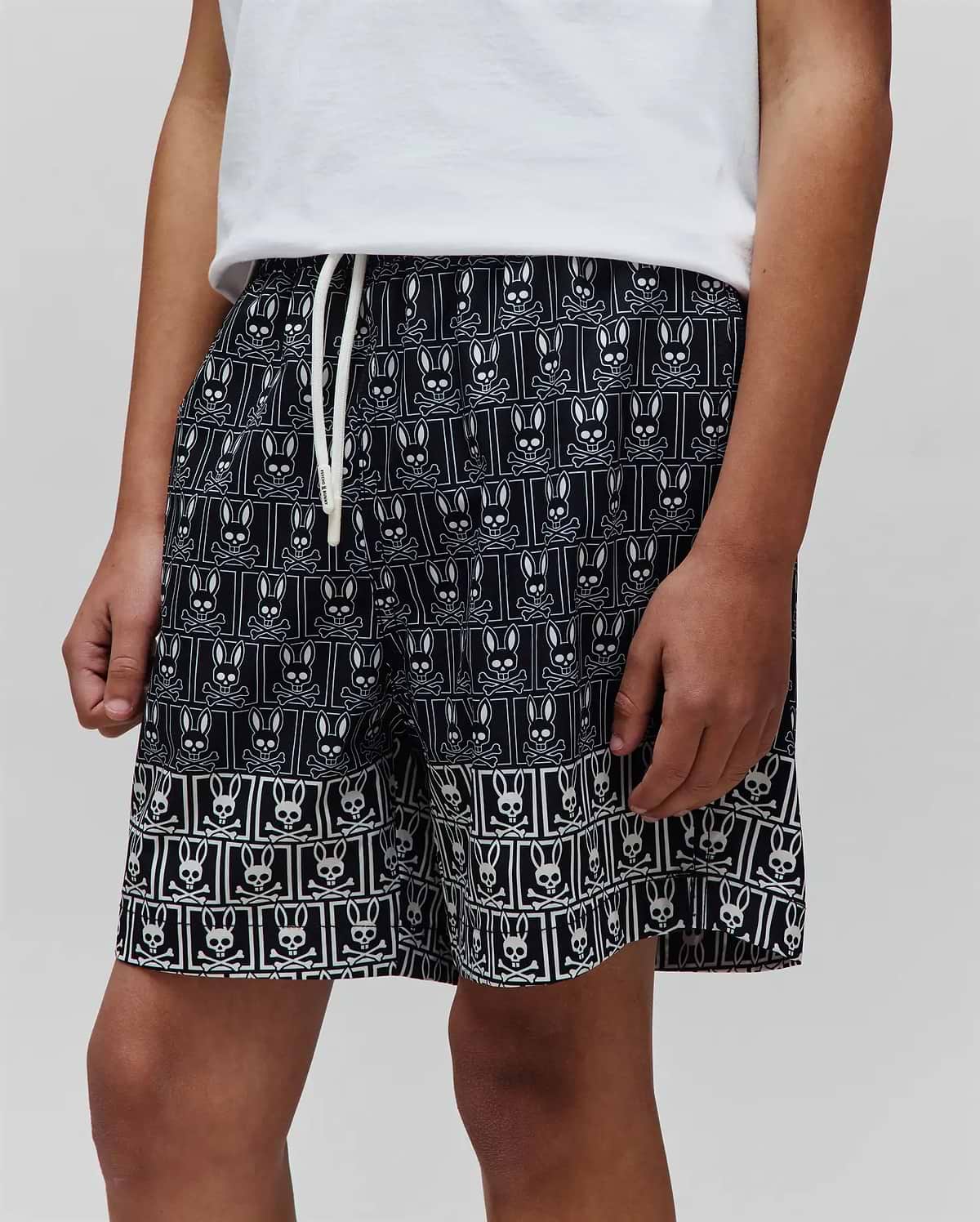 Kids Keon Swim Trunk, black with white all-over Psycho Bunny skull and crossbones grid print, relaxed fit, smooth quick-dry fabric, and white drawstring. (2)