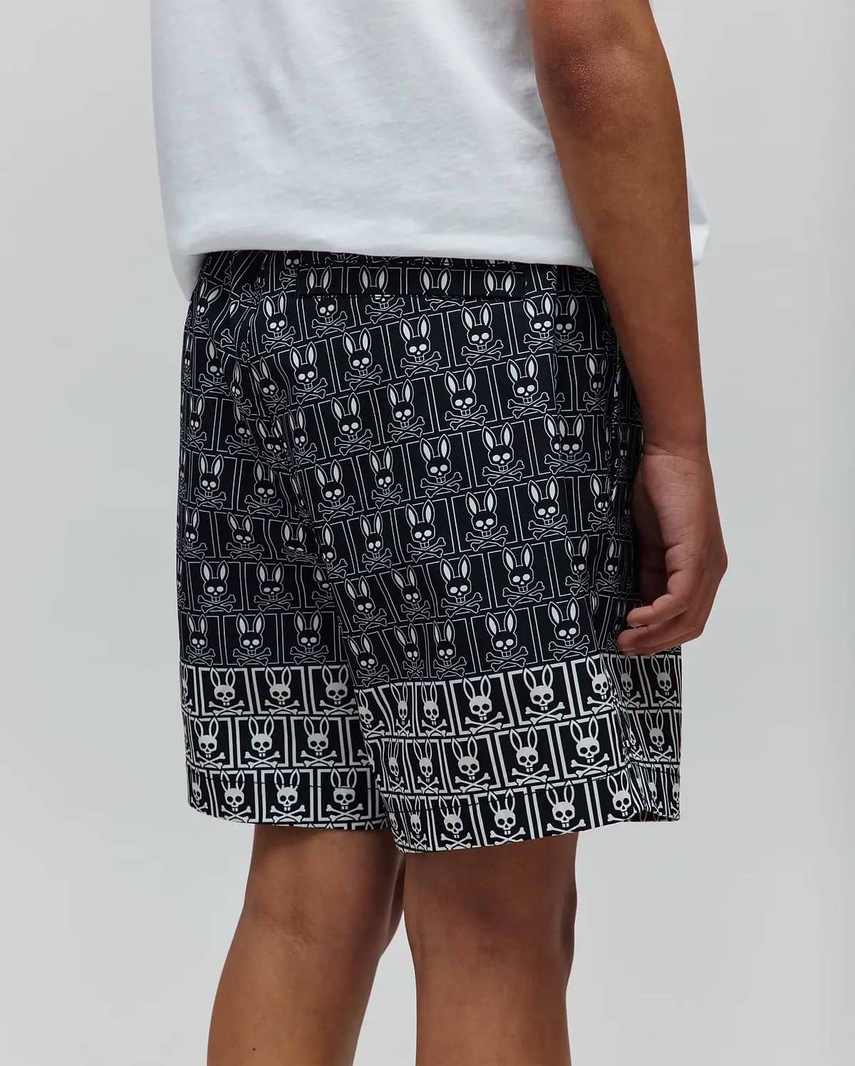 Kids Keon Swim Trunk featuring a relaxed fit, black fabric with an all-over white Psycho Bunny skull and crossbones logo pattern, and a distinct border design at the hem. (3)