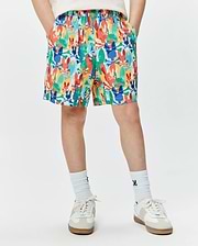 Kids Tanner Swim Trunk with a vibrant multi-color all-over print of Psycho Bunny skull and crossbones logos in red, orange, yellow, green, blue, and white, featuring a relaxed fit and elastic waistband.