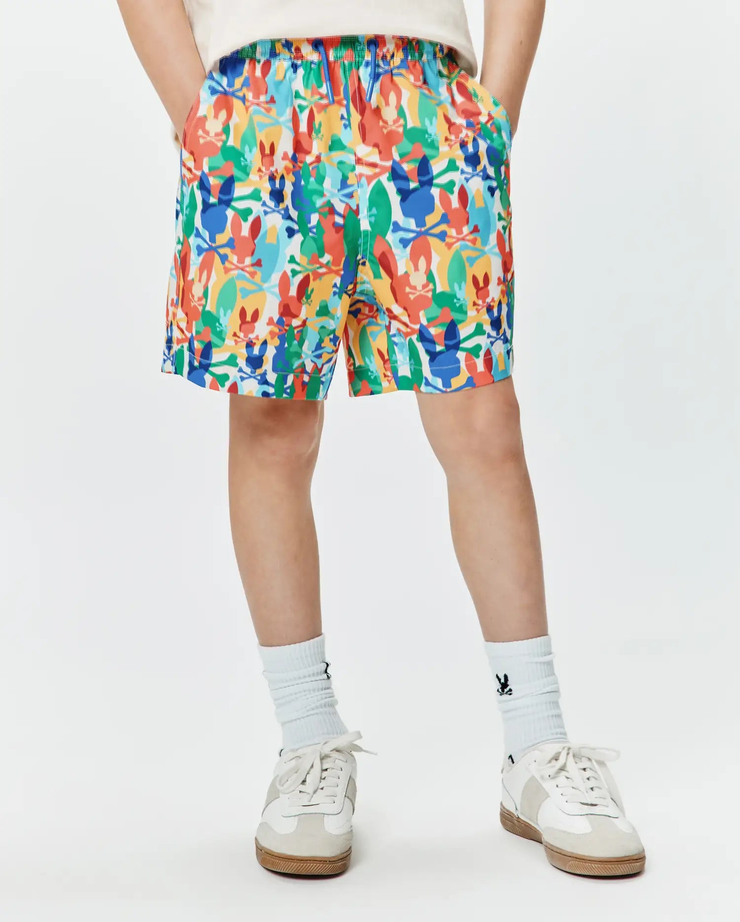 Kids Tanner Swim Trunk with a vibrant multi-color all-over print of Psycho Bunny skull and crossbones logos in red, orange, yellow, green, blue, and white, featuring a relaxed fit and elastic waistband.