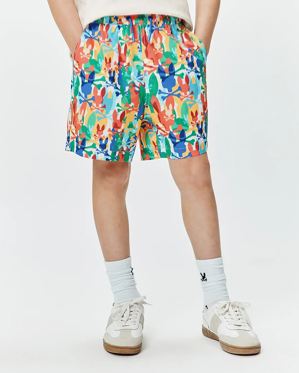 Kids Tanner Swim Trunk with a vibrant multi-color all-over print of Psycho Bunny skull and crossbones logos in red, orange, yellow, green, blue, and white, featuring a relaxed fit and elastic waistband.
