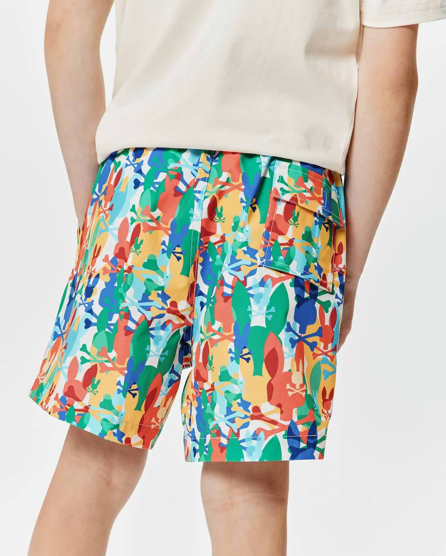 Kids Tanner Swim Trunk in vibrant multi-color, featuring an all-over abstract print of Psycho Bunny skull logos and bunny silhouettes, with a relaxed fit and a cargo pocket.