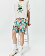 Ecru jersey t-shirt with a large green Psycho Bunny skull logo wearing sunglasses on the chest, paired with multicolor KIDS TANNER SWIM TRUNK featuring an all-over Psycho Bunny skull print.
