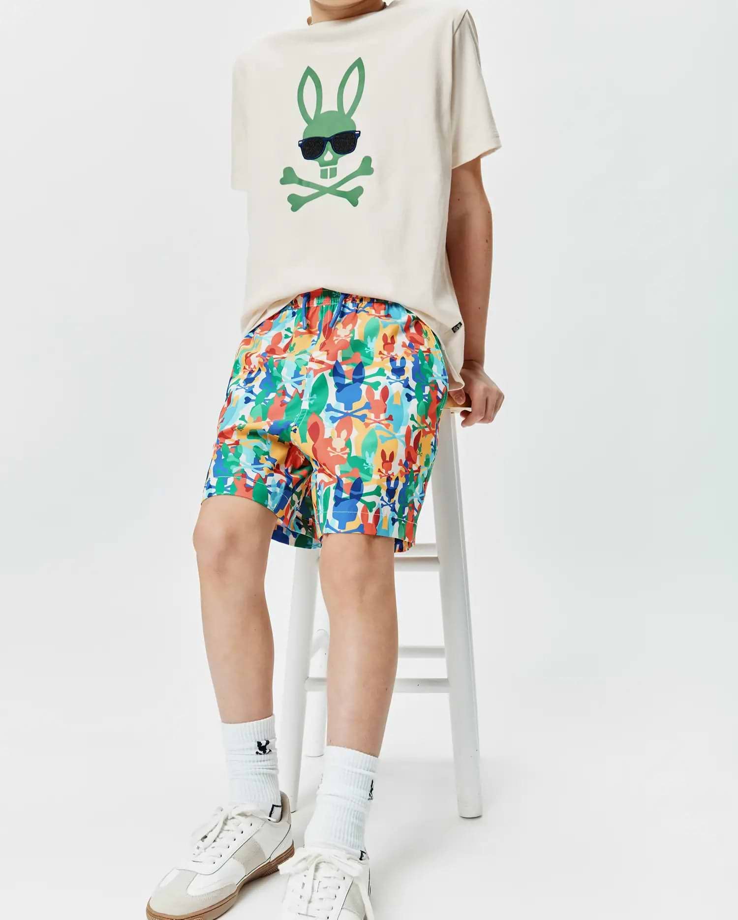 Ecru jersey t-shirt with a large green Psycho Bunny skull logo wearing sunglasses on the chest, paired with multicolor KIDS TANNER SWIM TRUNK featuring an all-over Psycho Bunny skull print.