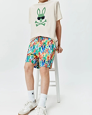 Ecru jersey t-shirt with a large green Psycho Bunny skull logo wearing sunglasses on the chest, paired with multicolor KIDS TANNER SWIM TRUNK featuring an all-over Psycho Bunny skull print.