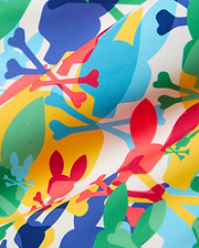 Kids Tanner Swim Trunk featuring a vibrant all-over print of overlapping Psycho Bunny skull and crossbones logos in red, blue, yellow, and green on a smooth white fabric.