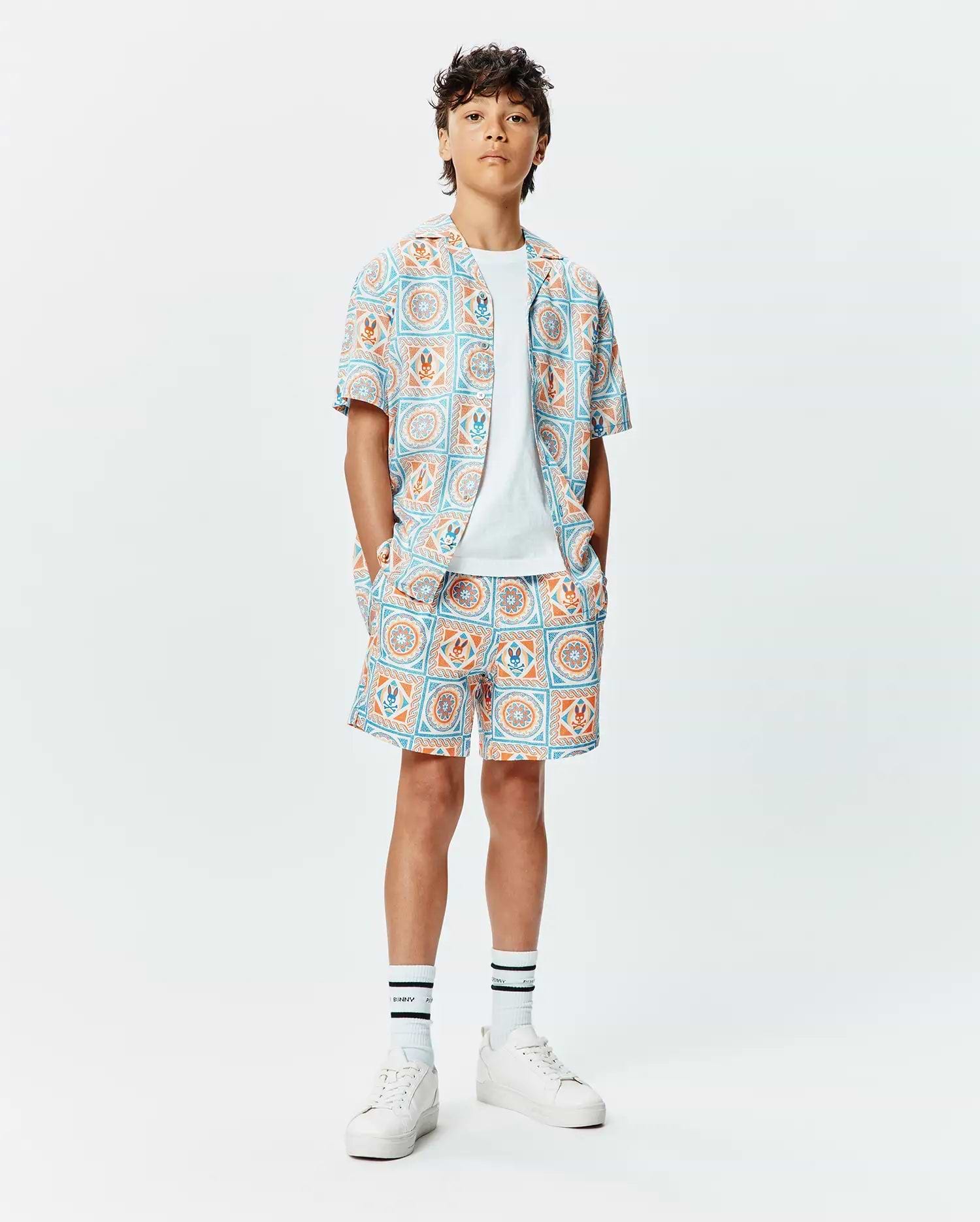 Kids Frank Swim Trunk and matching short-sleeve shirt in a relaxed fit, featuring a vibrant light blue and orange geometric tile pattern with integrated small Psycho Bunny skull logos throughout the smooth fabric. (4)