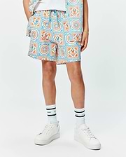 Kids Frank Swim Trunk in white with a vibrant blue and orange mosaic pattern, featuring repeated Psycho Bunny skull logos and a bright blue drawstring, in a relaxed fit. (1)