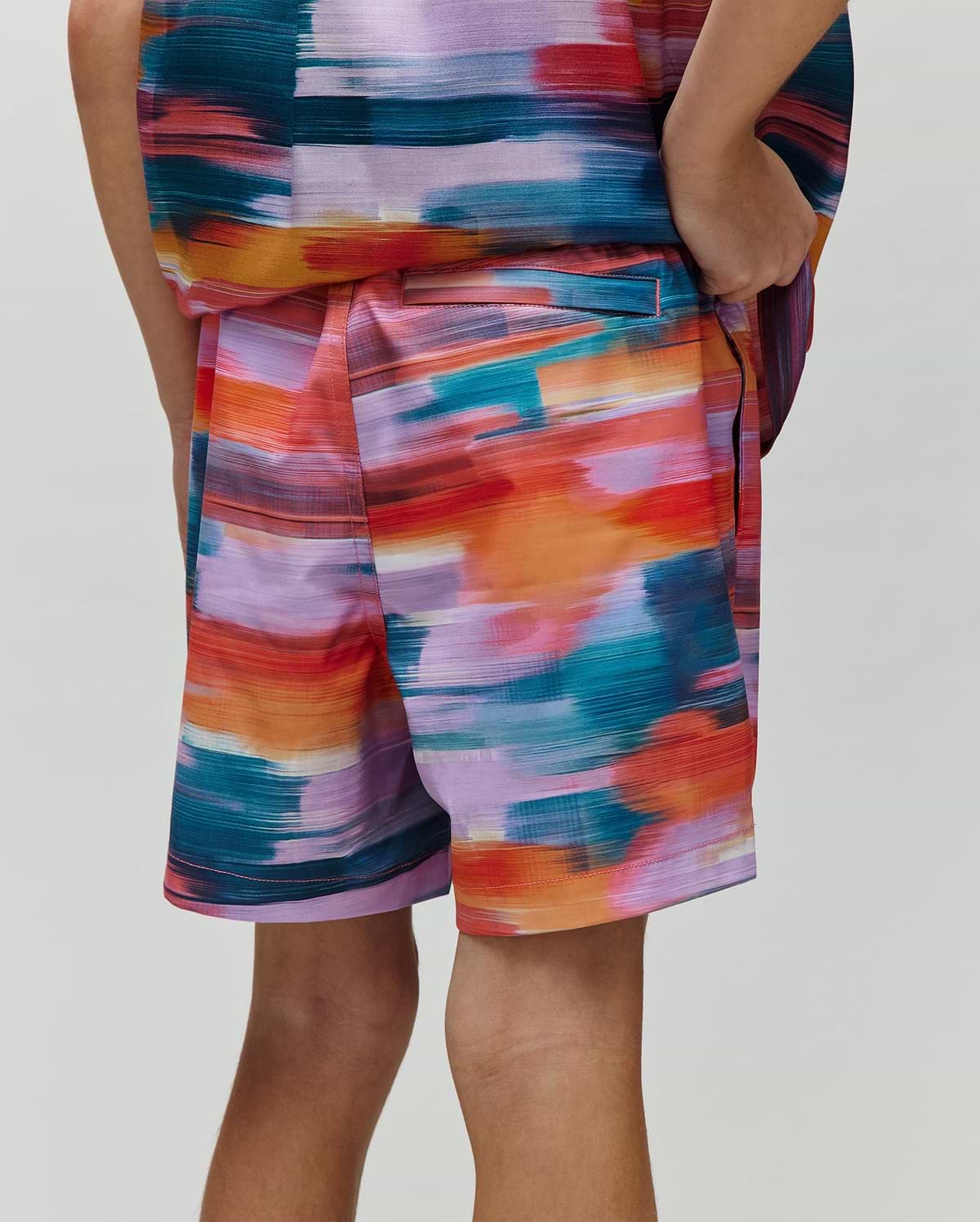 Kids Raphael Swim Trunk, a Psycho Bunny piece, showcasing a vibrant multi-color brushstroke pattern in teal, orange, red, purple, and pink, with a relaxed fit and smooth fabric.