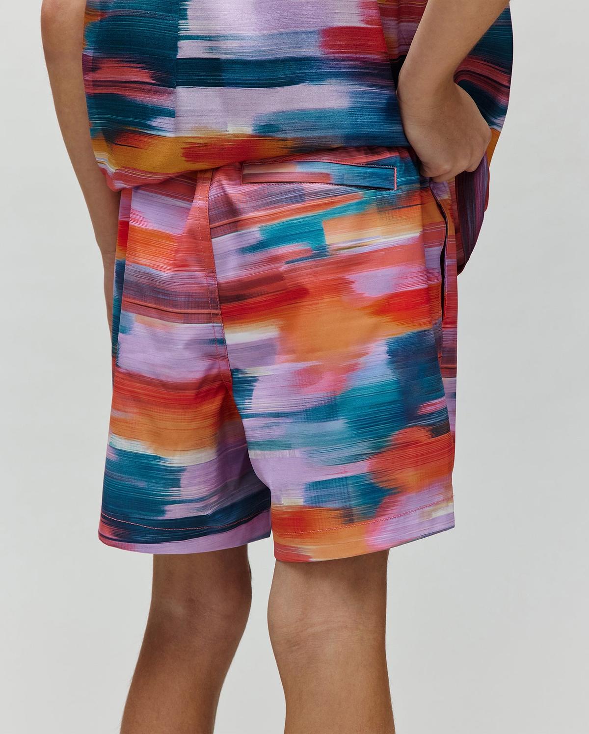 Kids Raphael Swim Trunk, a Psycho Bunny piece, showcasing a vibrant multi-color brushstroke pattern in teal, orange, red, purple, and pink, with a relaxed fit and smooth fabric.