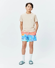 Beige jersey t-shirt with a small white embroidered Psycho Bunny skull logo, paired with Kids Ray Swim Trunk 6 featuring a vibrant blue wave, orange sunset, and bunny skull surfboard print.