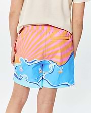 Kids Ray Swim Trunk 6, featuring a vibrant pink and orange sunburst pattern, blue waves with small Psycho Bunny skull logos wearing goggles, a back pocket, and a relaxed fit.