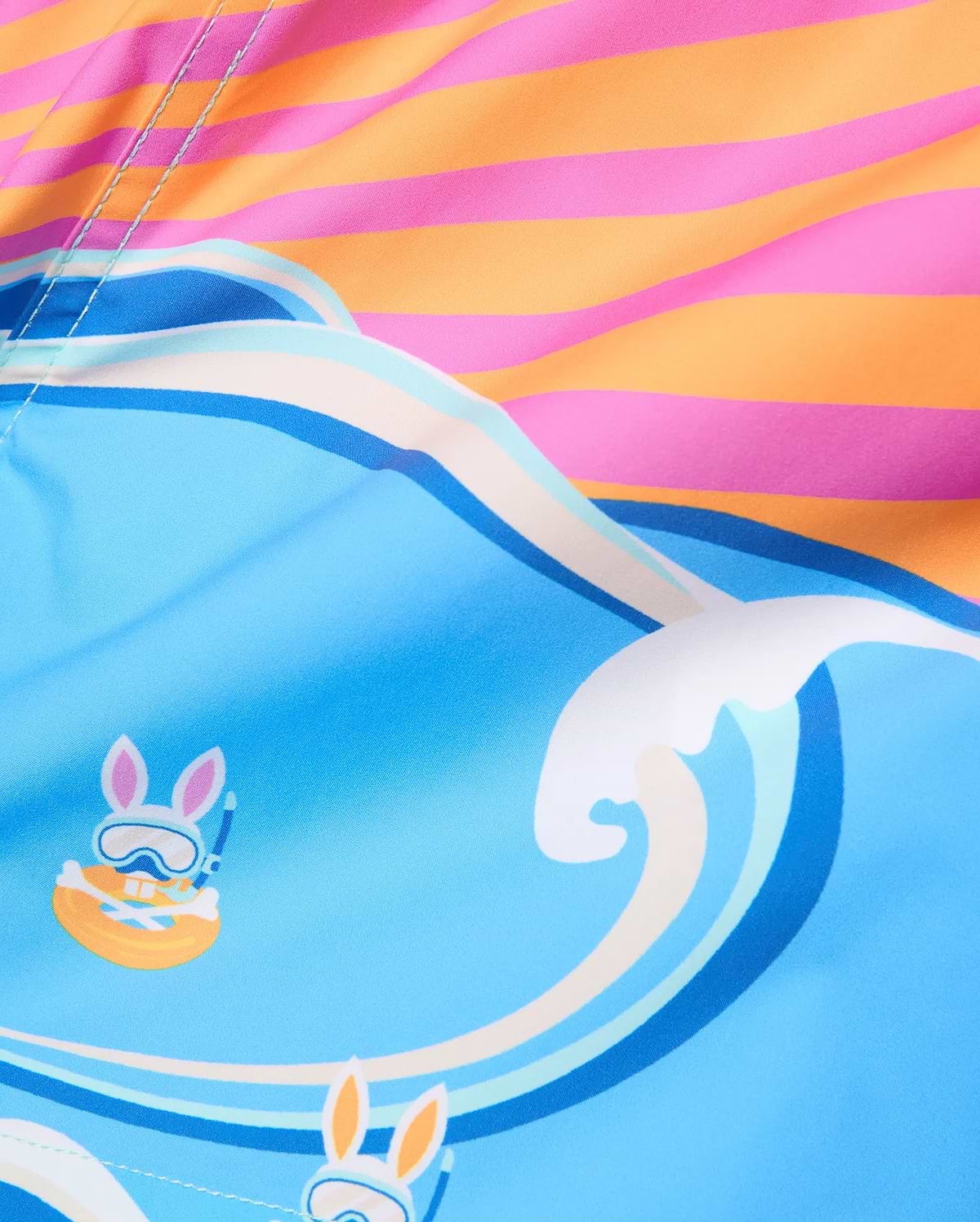 Kids Ray Swim Trunk 6, a vibrant blue swim trunk with a playful wave pattern, featuring repeated Psycho Bunny skull graphics wearing snorkel gear, accented by a bold pink and orange striped top.