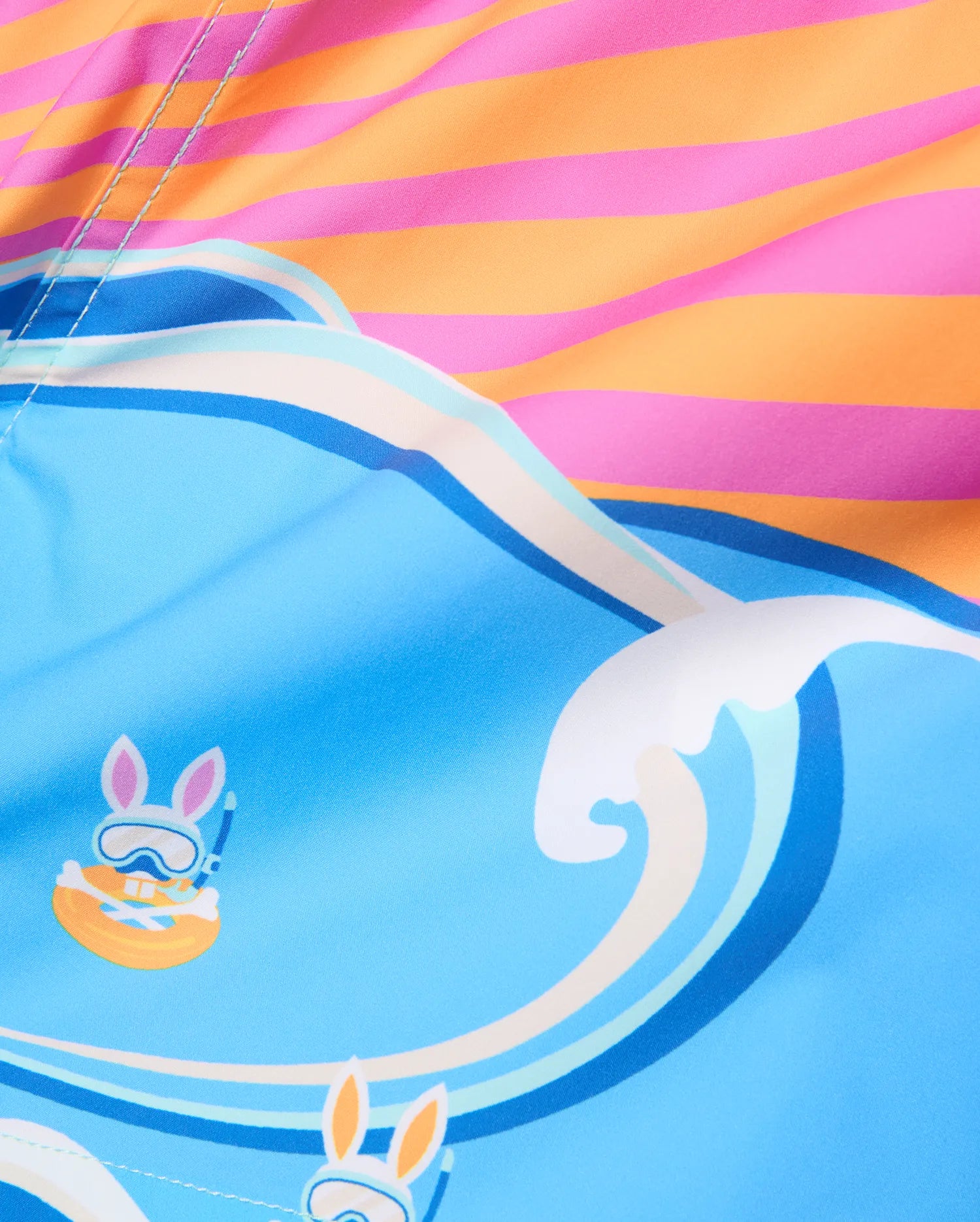 Kids Ray Swim Trunk 6, a vibrant blue swim trunk with a playful wave pattern, featuring repeated Psycho Bunny skull graphics wearing snorkel gear, accented by a bold pink and orange striped top.