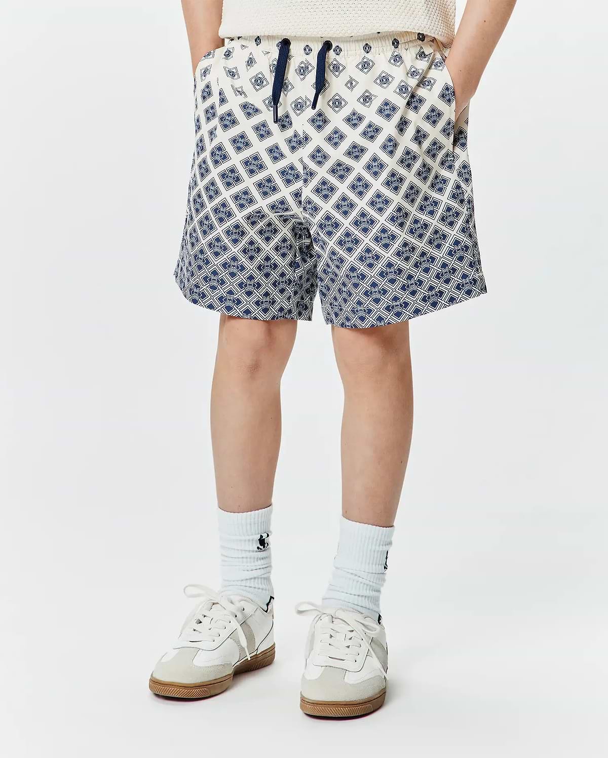 Kids Tobias Swim Trunk, cream with a navy blue all-over geometric pattern of the iconic Psycho Bunny skull logo, relaxed fit, smooth quick-dry fabric, and a navy drawstring. (1)