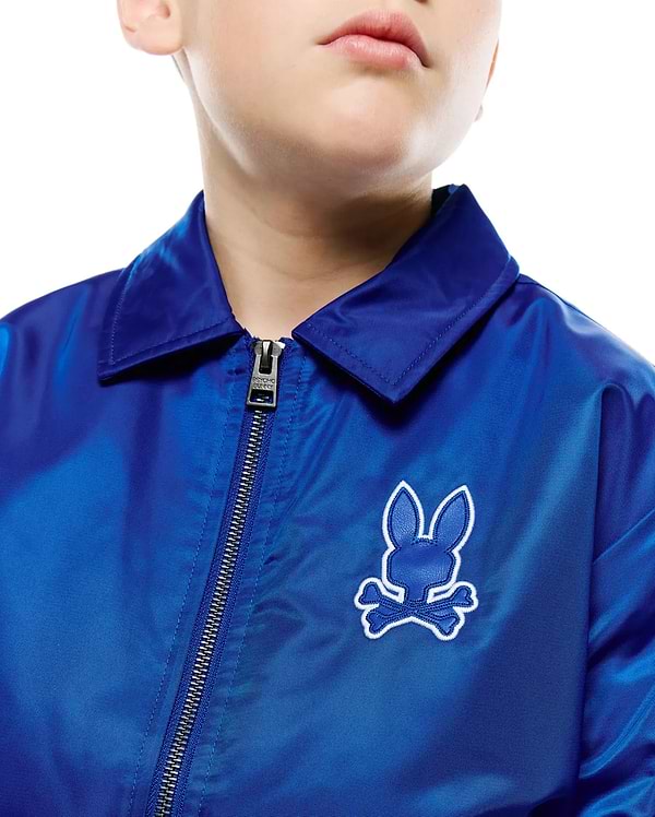 Kids Nathaniel Satin Coach Jacket in royal blue satin, featuring a collared neck, full silver zipper with Psycho Bunny pull, and an embroidered royal blue bunny skull logo with white outline on the left chest.
