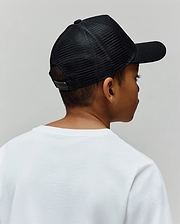 Black mesh back Kids Adamo Trucker Cap featuring a structured solid front panel, curved brim, and adjustable snapback closure, worn with a classic fit plain white jersey knit crew neck t-shirt.