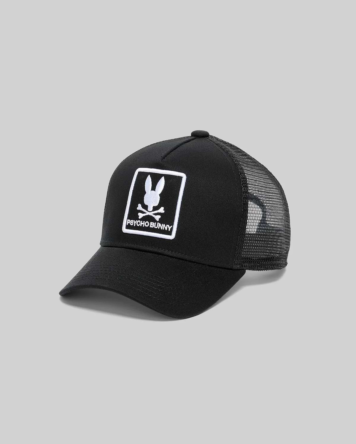 Black Kids Adamo Trucker Cap featuring a prominent white embroidered Psycho Bunny skull logo and text within a square patch on the twill front panel, complemented by a breathable mesh back.