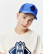 Classic fit cream jersey t-shirt with a large navy blue embroidered Psycho Bunny skull logo on the chest, and a royal blue Kids Tobias Trucker Cap with mesh back and a navy embroidered bunny skull logo.